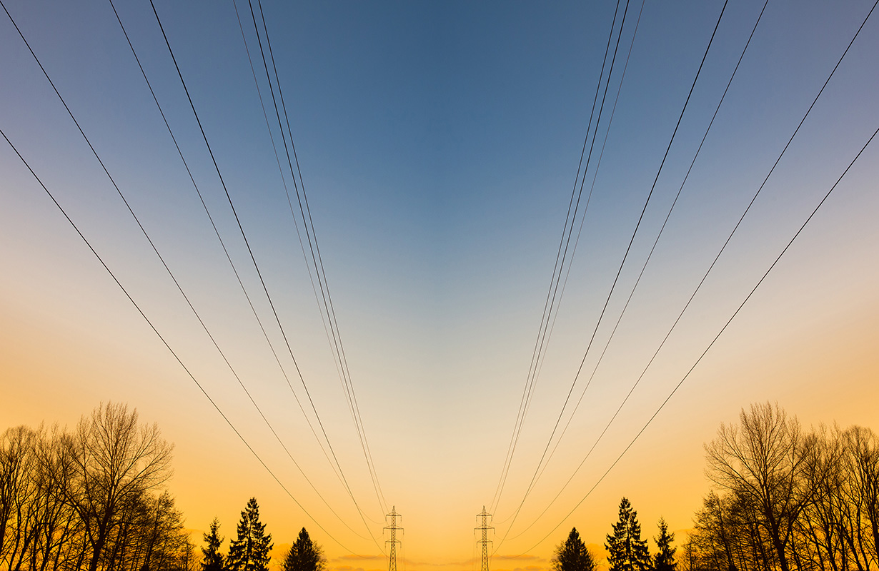 Luftledningar som syns mot en blå och gul himmel med grantoppar i bakgrunden